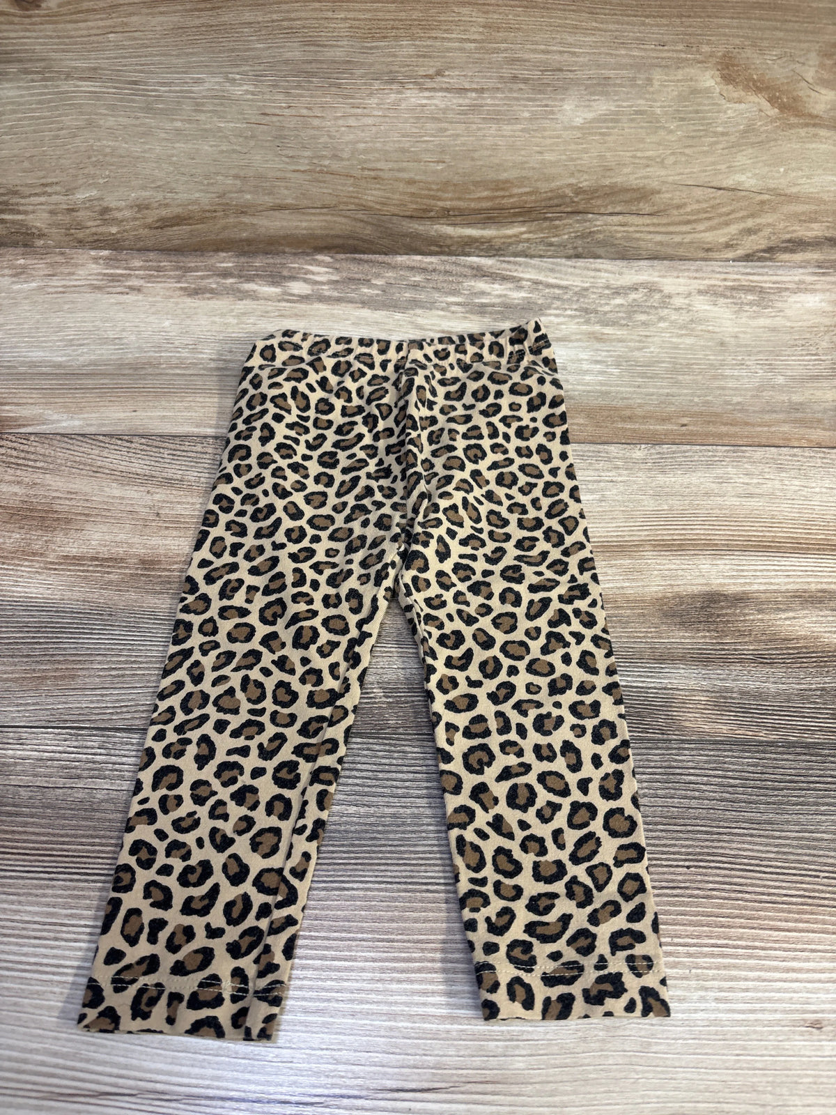 Flat lay of Old Navy leopard-print leggings 18-24M showing elastic waistband and tan-and-black pattern on light wood background