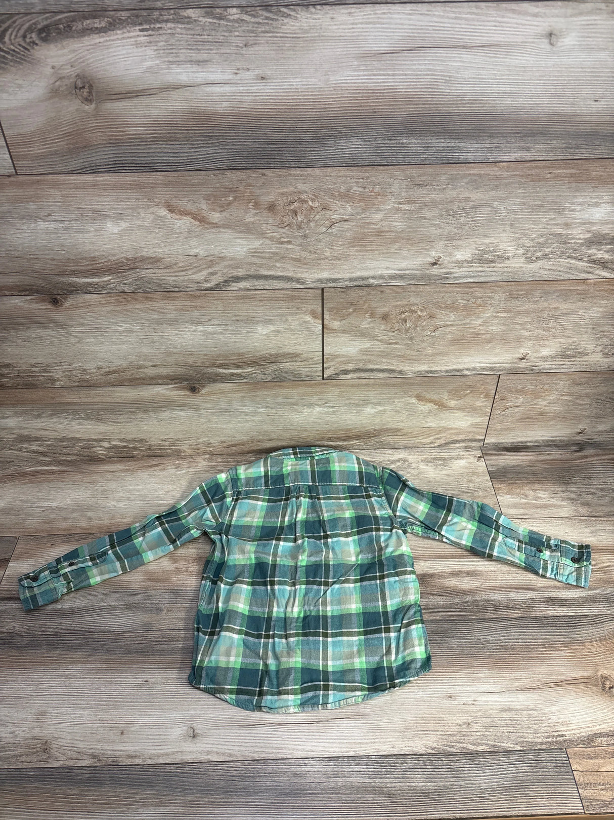 Green and blue plaid long-sleeve shirt laid flat on light brown wooden floor