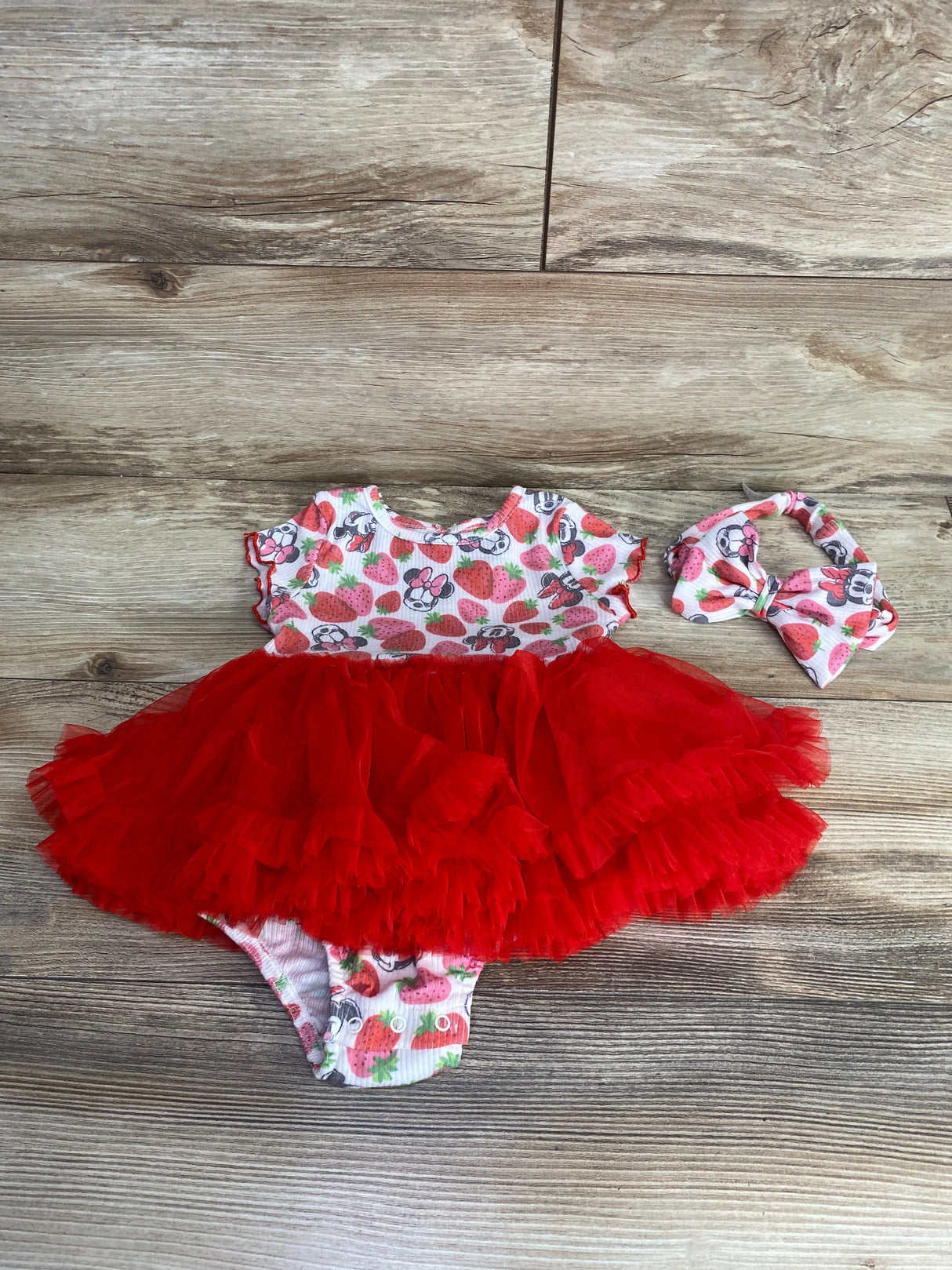 Baby girl red tutu dress with strawberry and Minnie Mouse print and matching headband on wooden floor