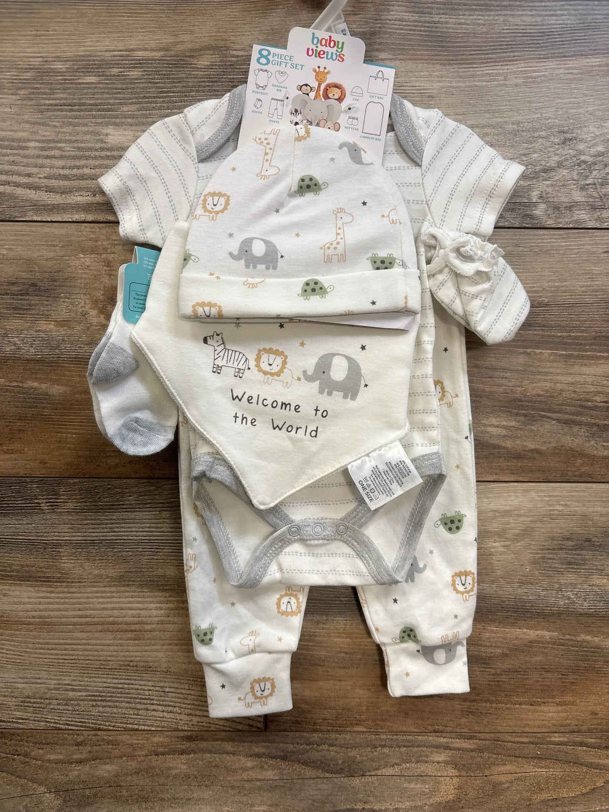Top-down view of Baby Views 6-piece gift set with hat, bib reading Welcome to the World, onesie, pants and socks on wood background
