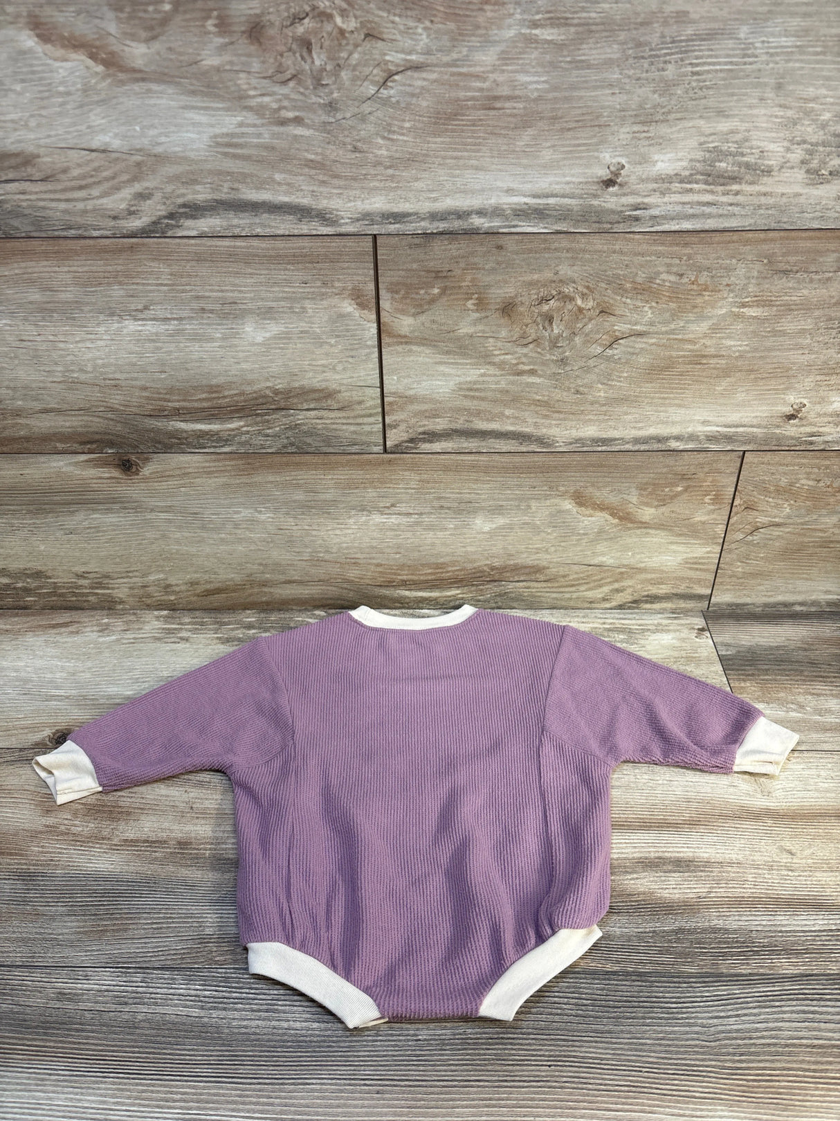 Purple ribbed baby onesie with white trim, laid flat on wood floor — kids clothing resale