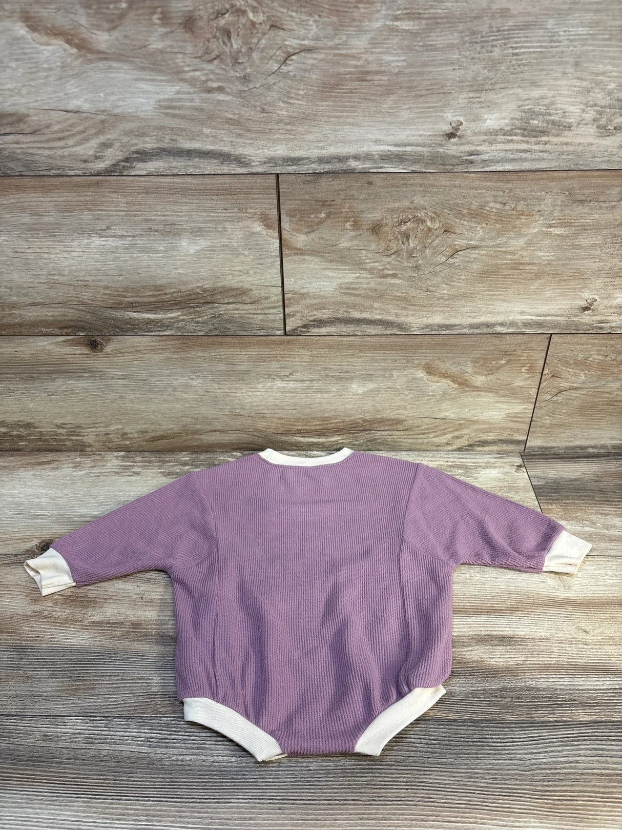 Purple ribbed baby onesie with white trim, laid flat on wood floor — kids clothing resale