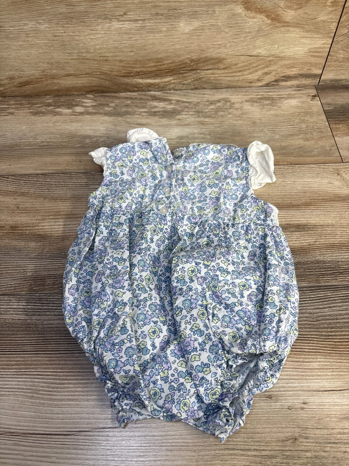 Back view of white floral embroidered bubble romper showcasing smocked waist and button-up back on a wood floor