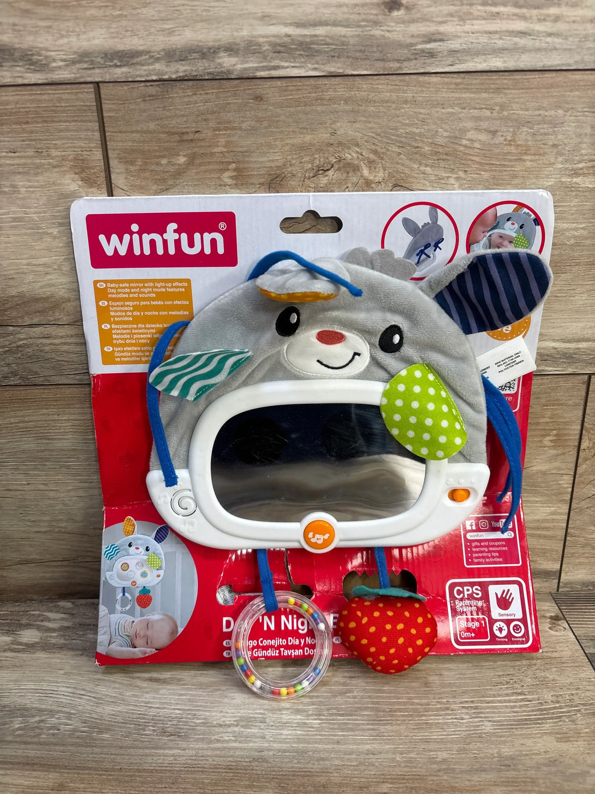 Front of Winfun Day & Night Bunny Pal showing gray plush bunny with mirror, beaded ring and strawberry toy on red backing