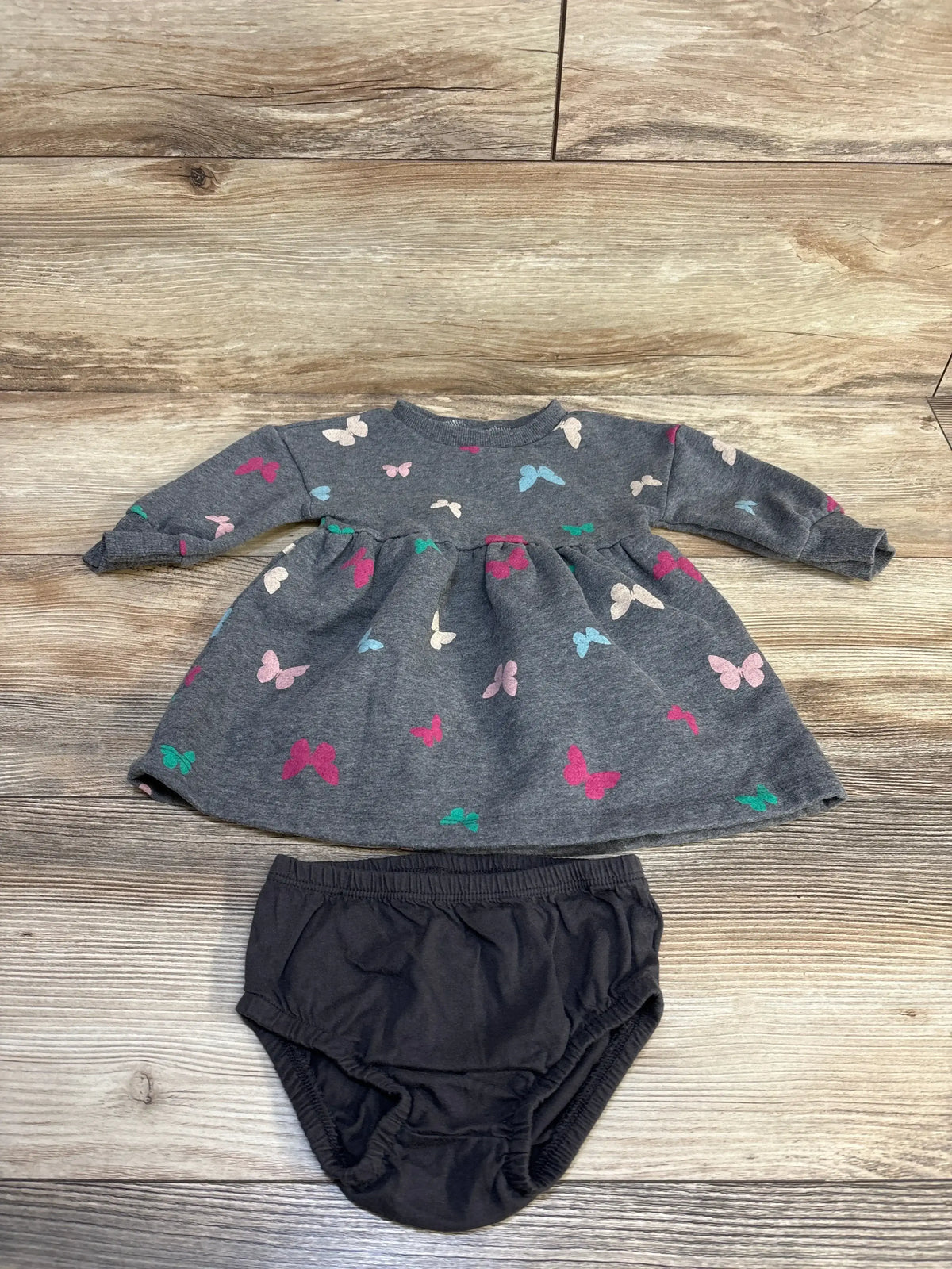 Gray butterfly print baby dress with black bloomers on wood floor