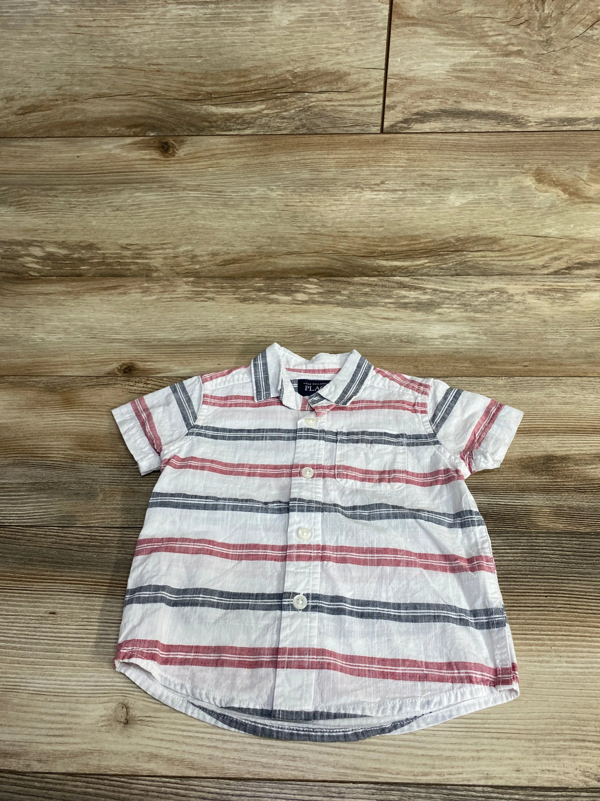 Short sleeve button-up baby shirt with red and blue stripes on a wooden background