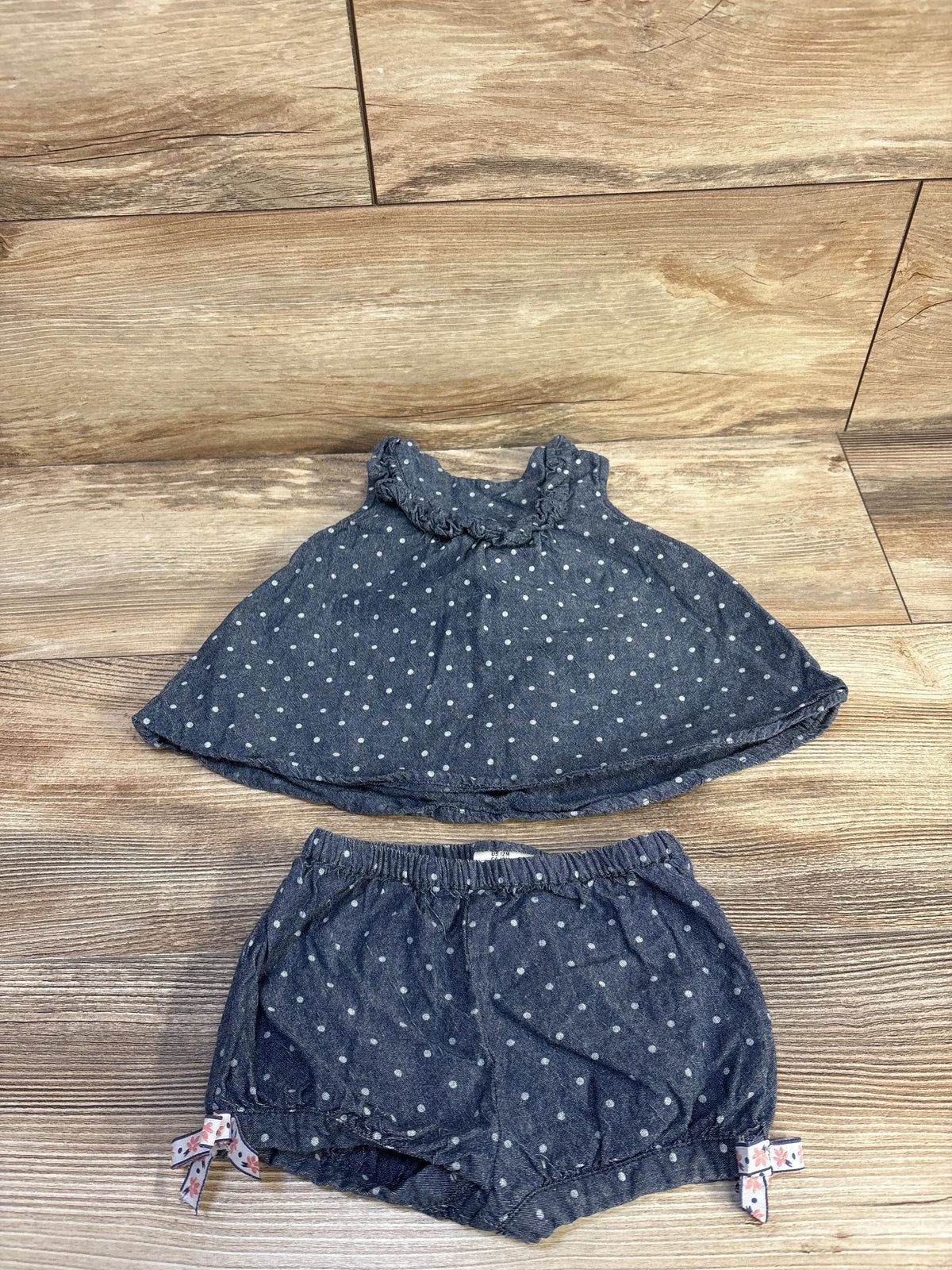 Flat lay of baby chambray polka dot sleeveless top and matching bloomers, 12m, showing ruffled collar and elastic waist on wood background