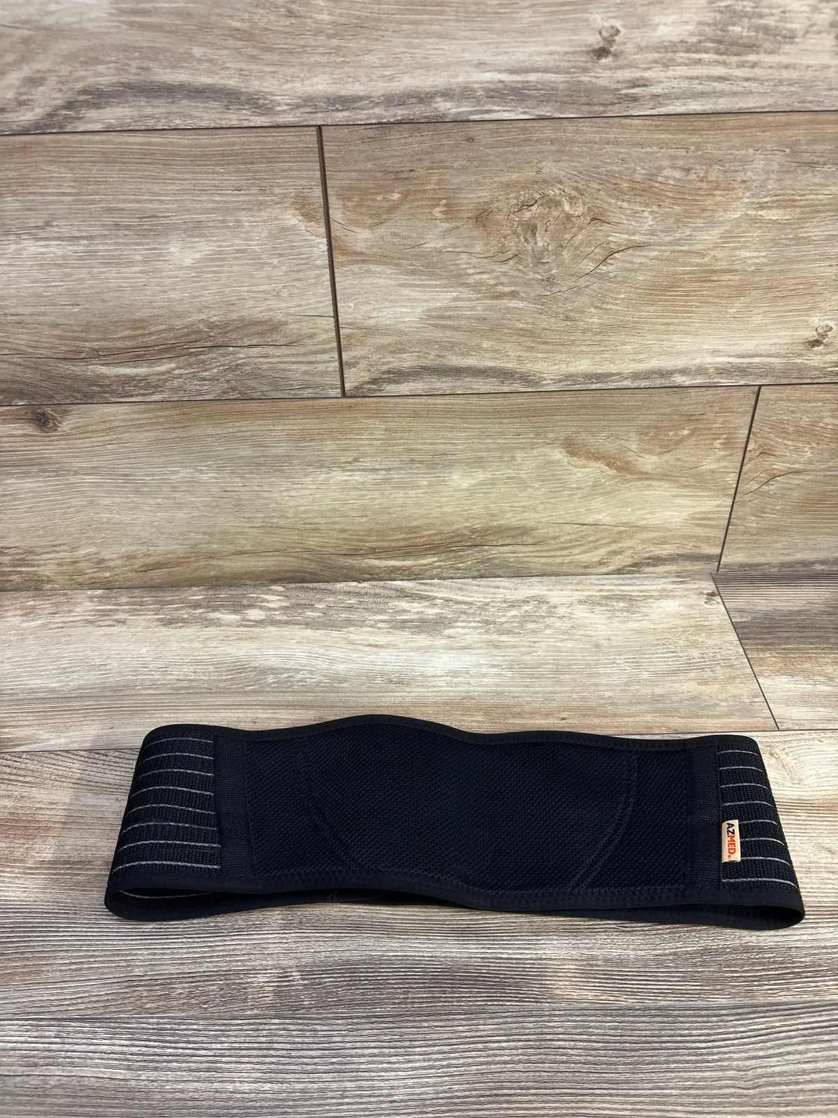 Flat-lay of AZMed maternity back support band showing breathable mesh panel and adjustable Velcro straps on wood floor