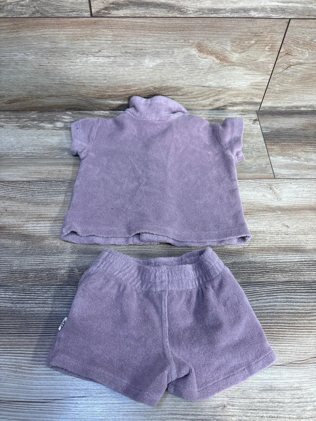 Flat lay of Easy Peasy purple terry cloth shirt and matching shorts showing short sleeves and elastic waistband on wood floor