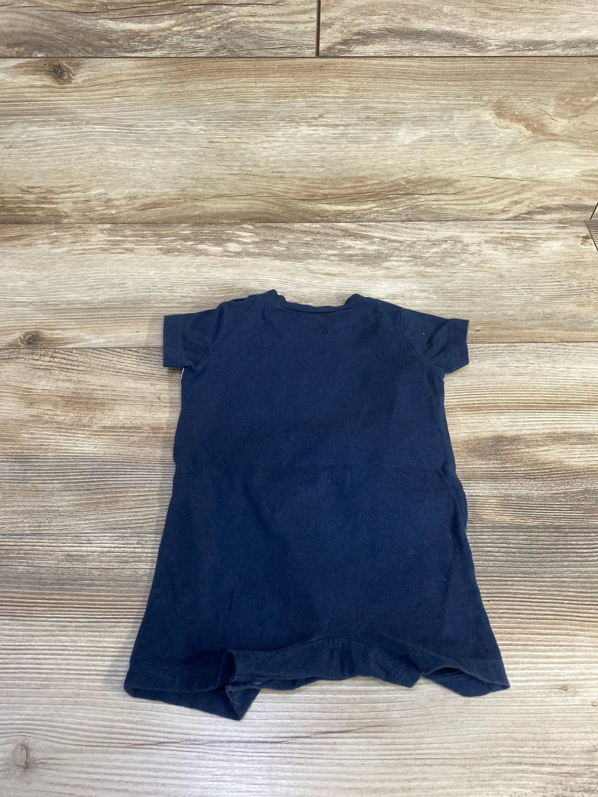 Back view of size 6 month black Nike shortie romper showing short sleeves and crew neckline on wood floor background
