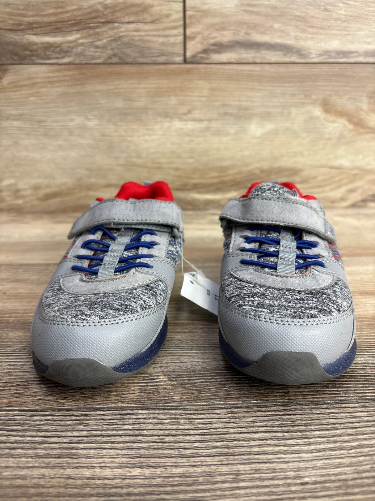 Pair of gray kids sneakers with blue laces and red interior on wooden floor background