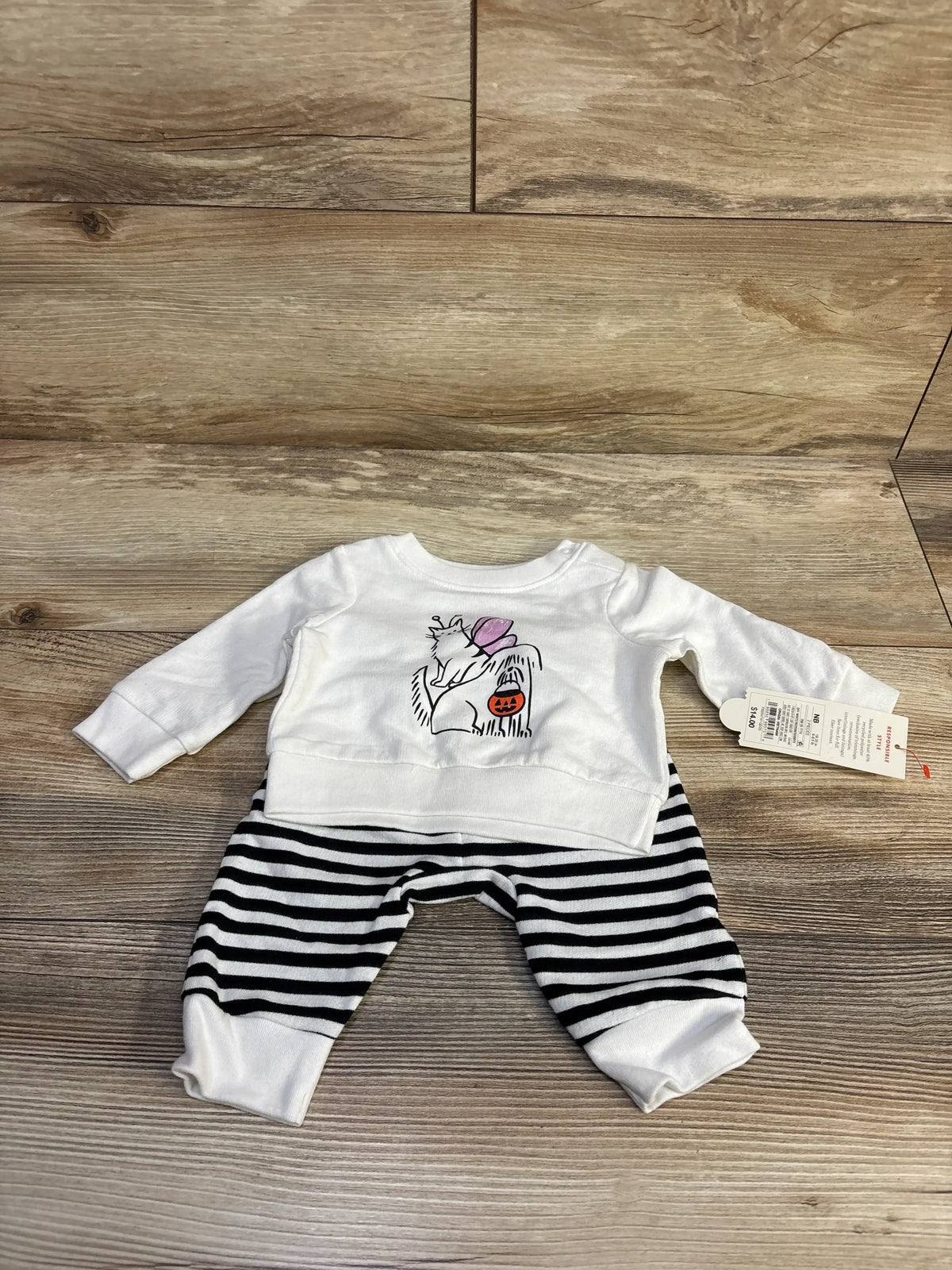 Flat lay of newborn 2-piece Halloween set: white sweatshirt with dog-and-cat graphic and black-and-white striped joggers on wood background
