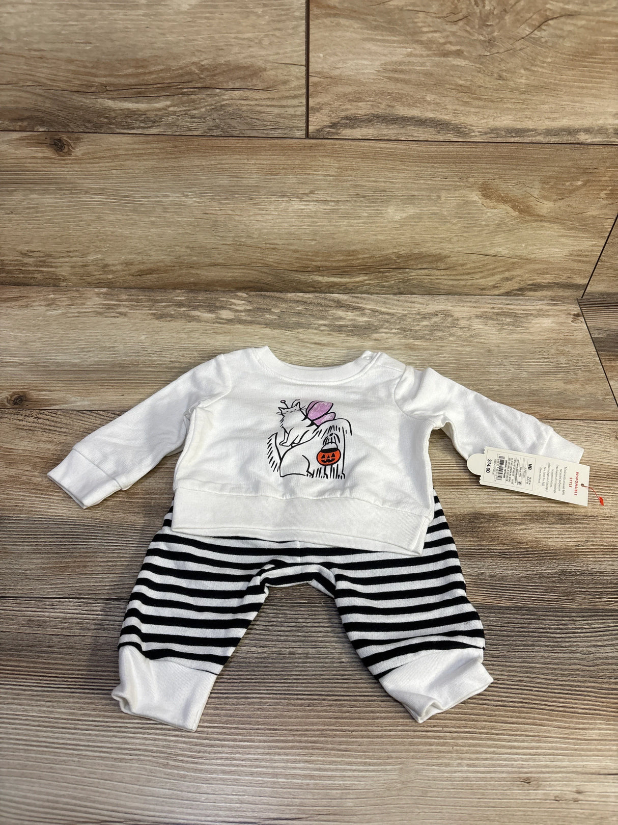 Flat lay of newborn 2-piece Halloween set: white sweatshirt with dog-and-cat graphic and black-and-white striped joggers on wood background