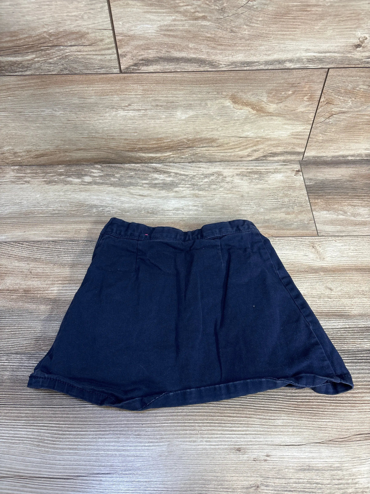 Flat lay of Children’s Place navy ponte knit button skort showcasing elastic waistband and slight A-line shape on wood floor background
