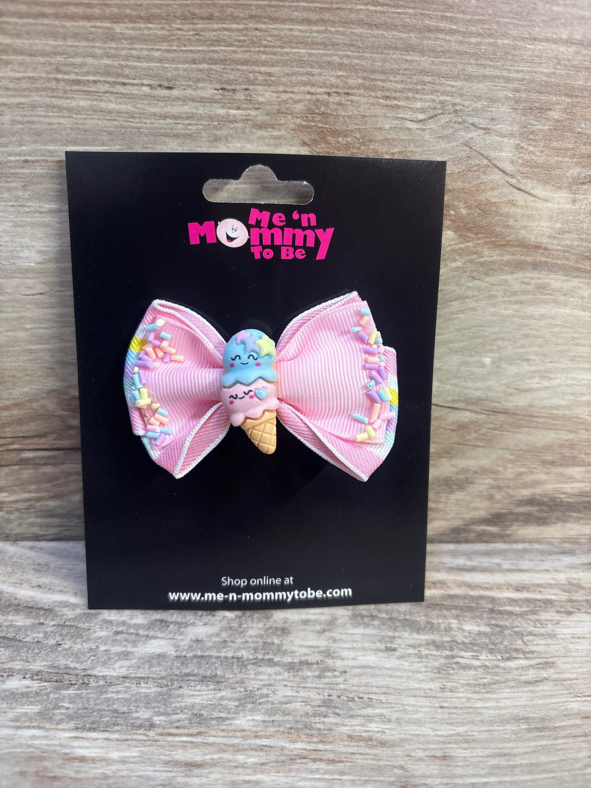 Front view of pink ribbon hair bow with smiling two-scoop ice cream applique and pastel sprinkle accents on a black display card