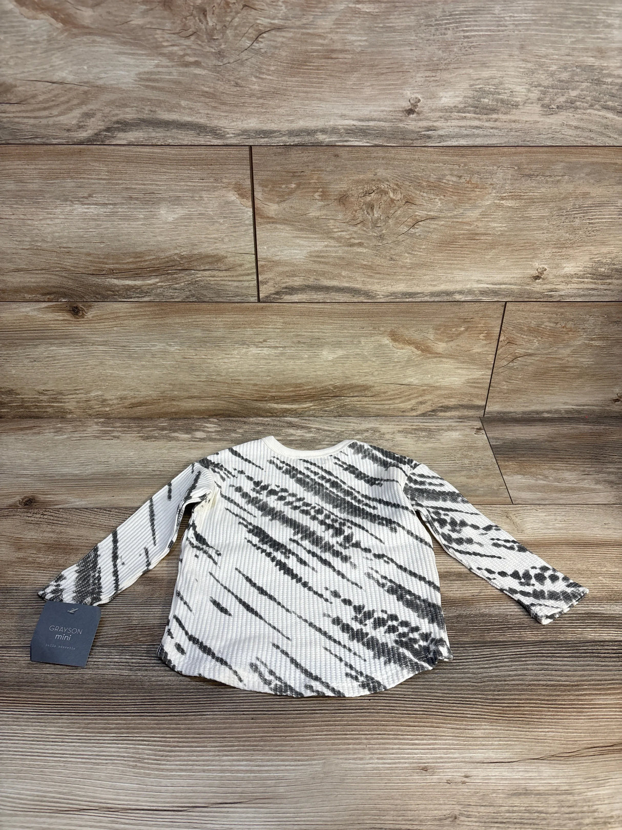 Long sleeve toddler shirt with black and white tie-dye pattern, laid on wood floor