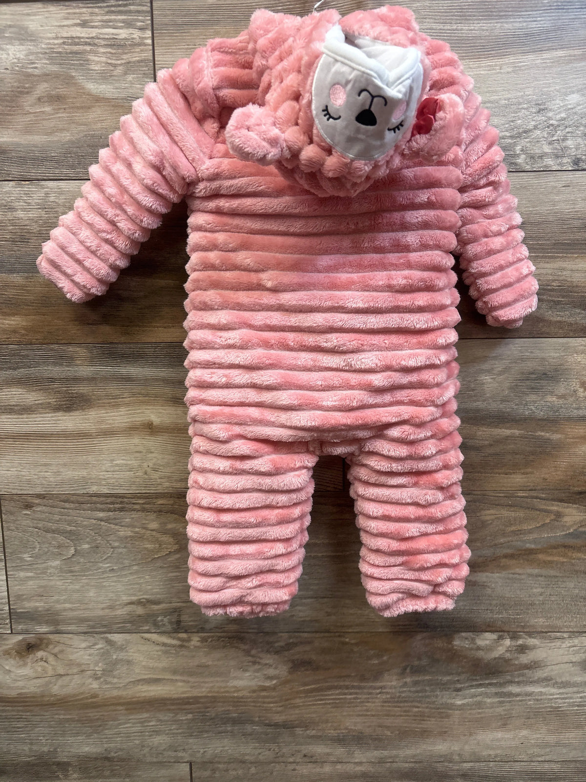 Front view of pink plush pram bunting showcasing ribbed texture and koala hood with a wood floor background