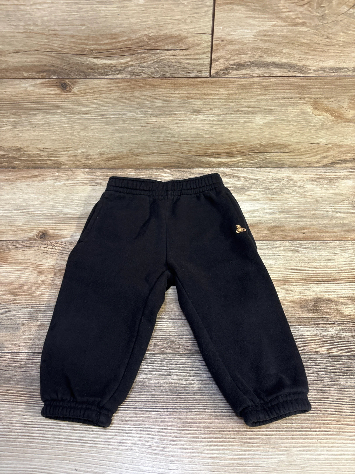 Flat lay of Baby Gap black pull-on baby joggers with elastic waistband and cuffs on wood background, size 12-18 months