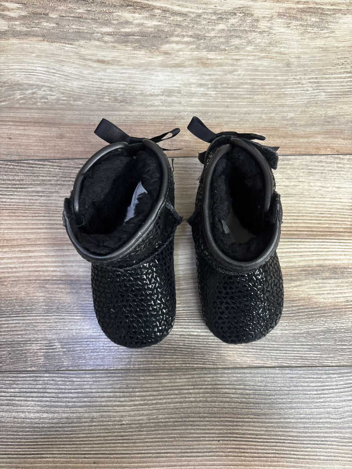 Pair of black textured baby boots with soft inner lining on wooden floor