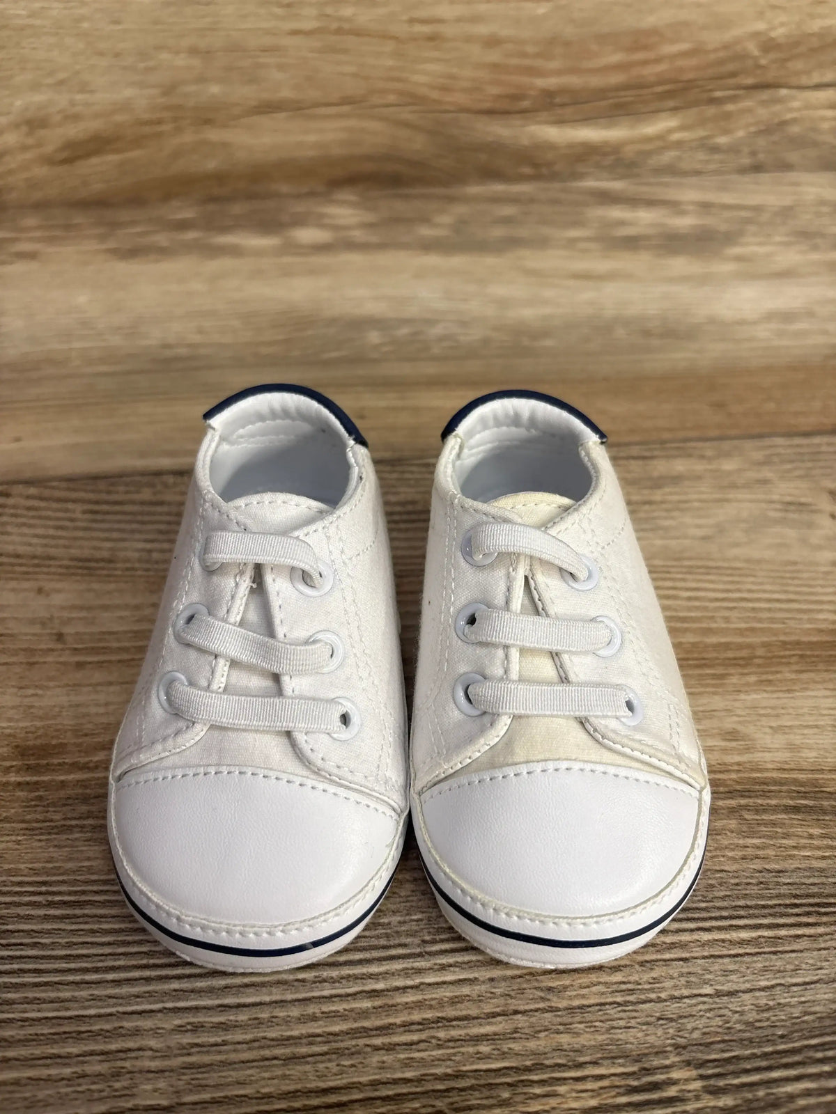 Pair of white baby shoes with navy accents and white laces on wooden surface