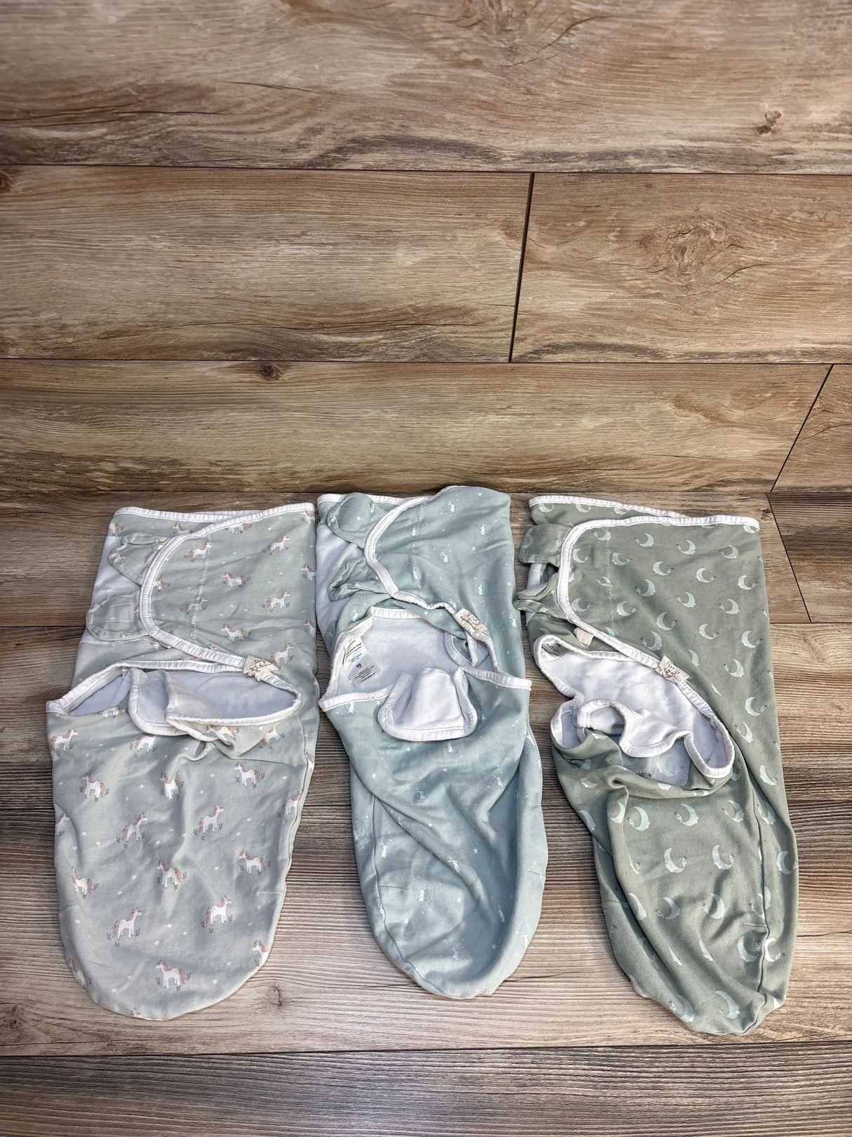 Three pastel baby swaddle blankets with animal and moon prints on wood floor