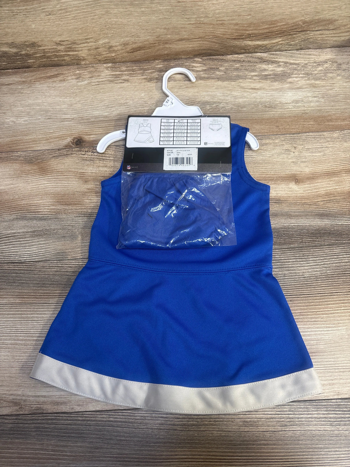 Blue toddler dress with white hem on hanger, packaged with matching blue underwear on wood background