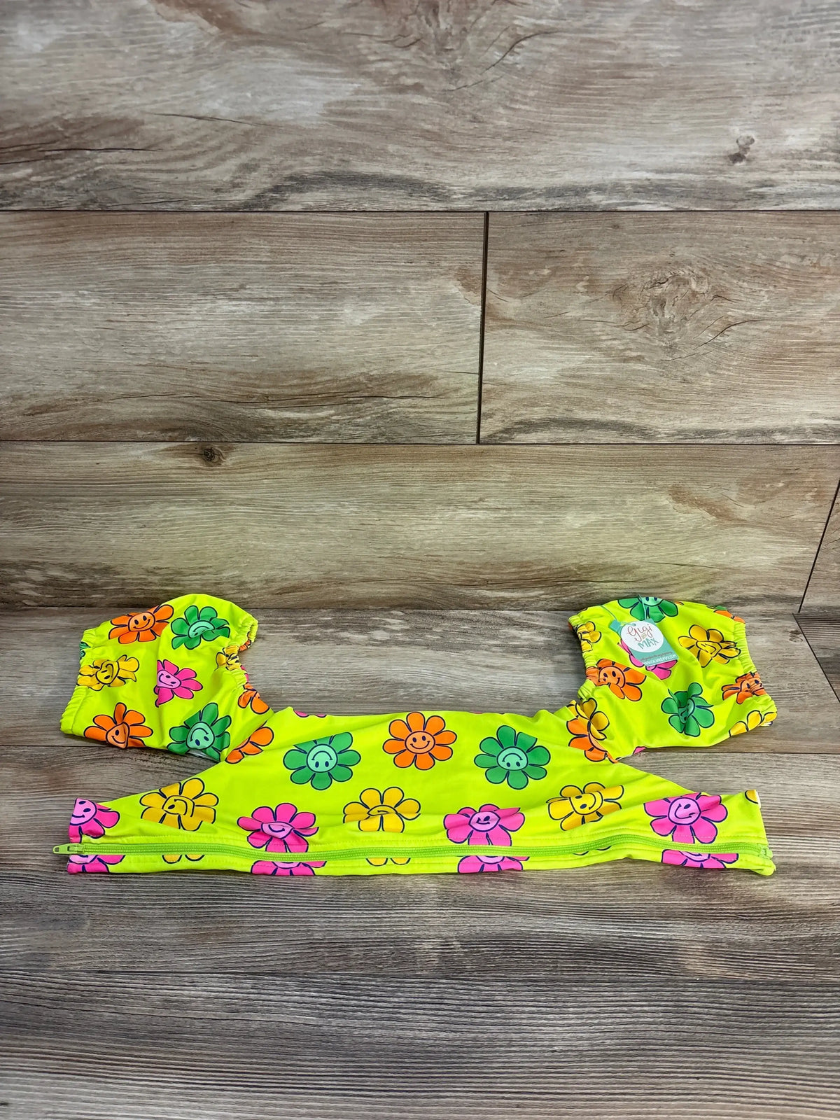 Flat lay of Gigi & Max Flower Floatie Cover in neon yellow with colorful smiley flowers and puff sleeves on wood background