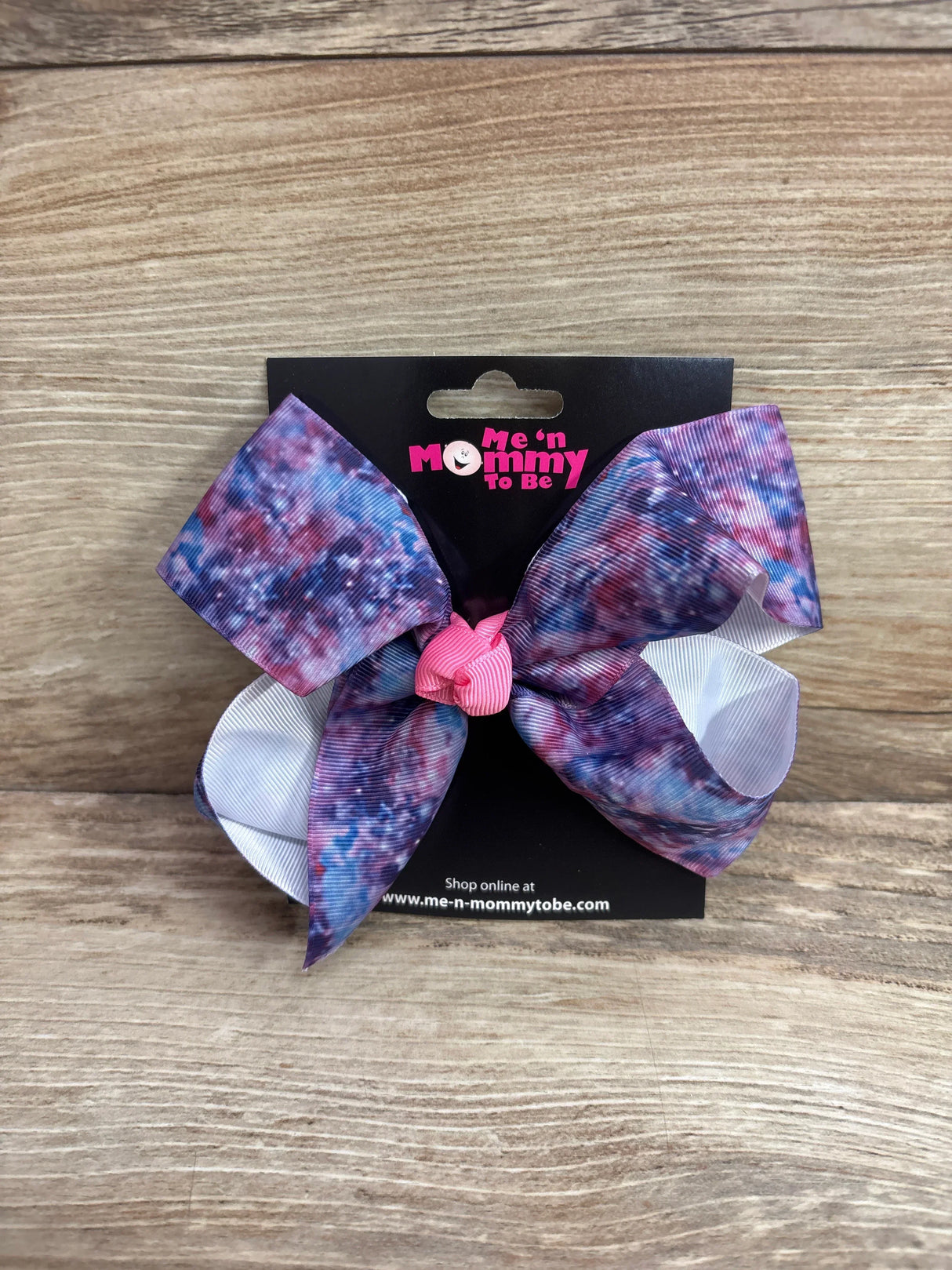 Front view of large hair bow in galaxy purple showing pink center knot and white loops on a black card over wood background