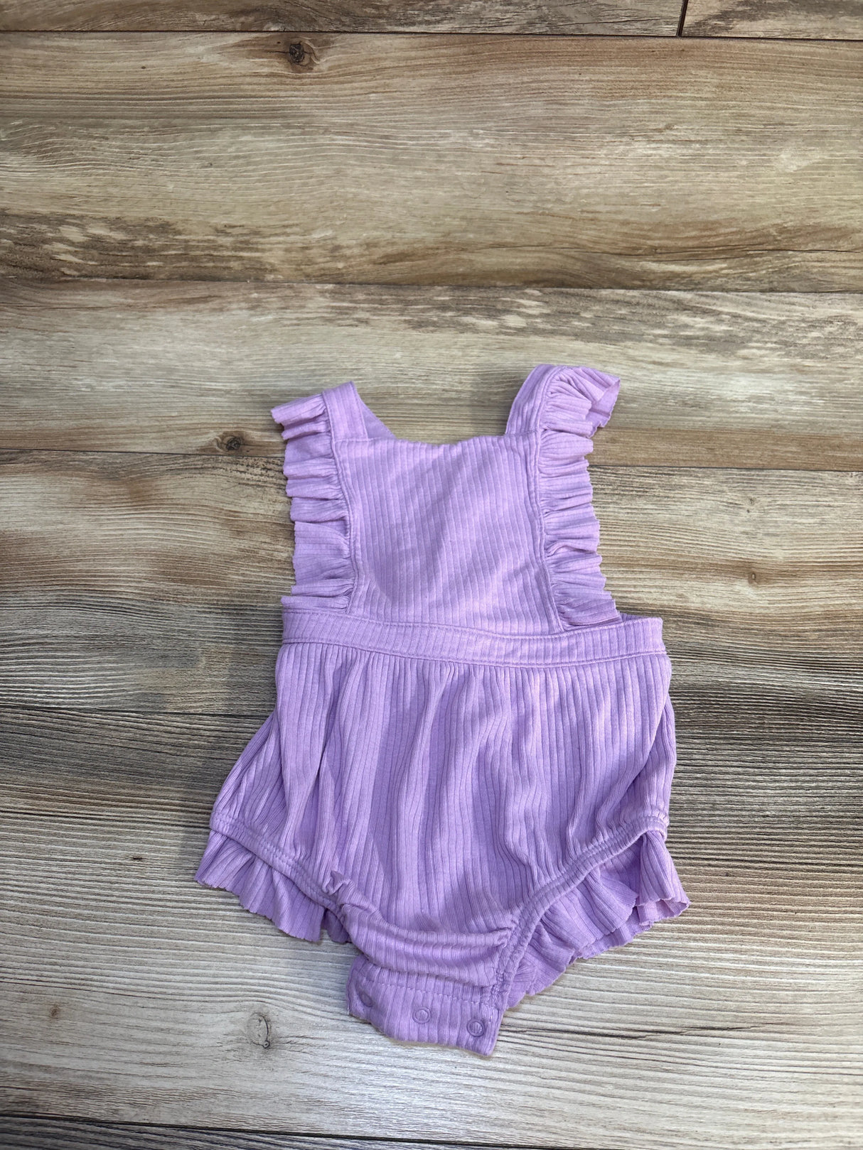 Flat lay of ribbed purple bubble romper size 18 months showing ruffled shoulder straps and snap crotch on wood background