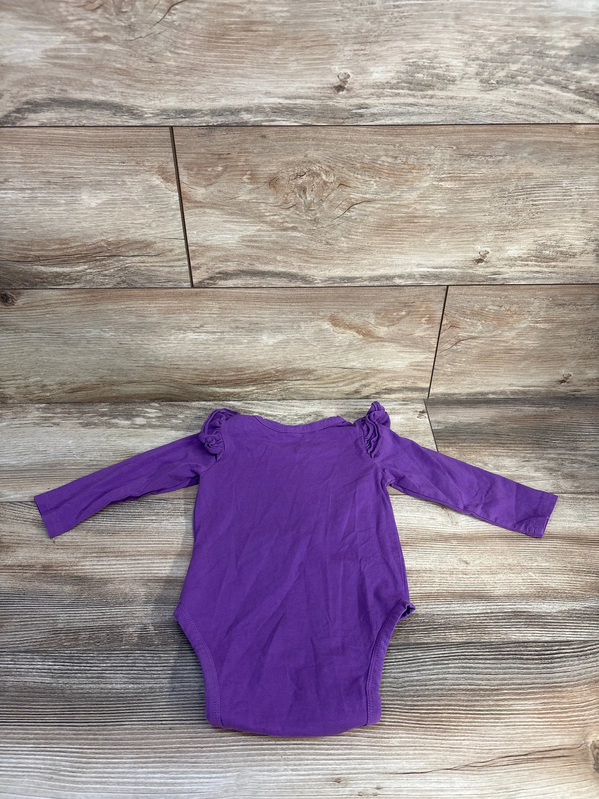 Front view of a purple long sleeve bodysuit for ages 12 to 18 months, showcasing ruffled shoulders on a wood floor