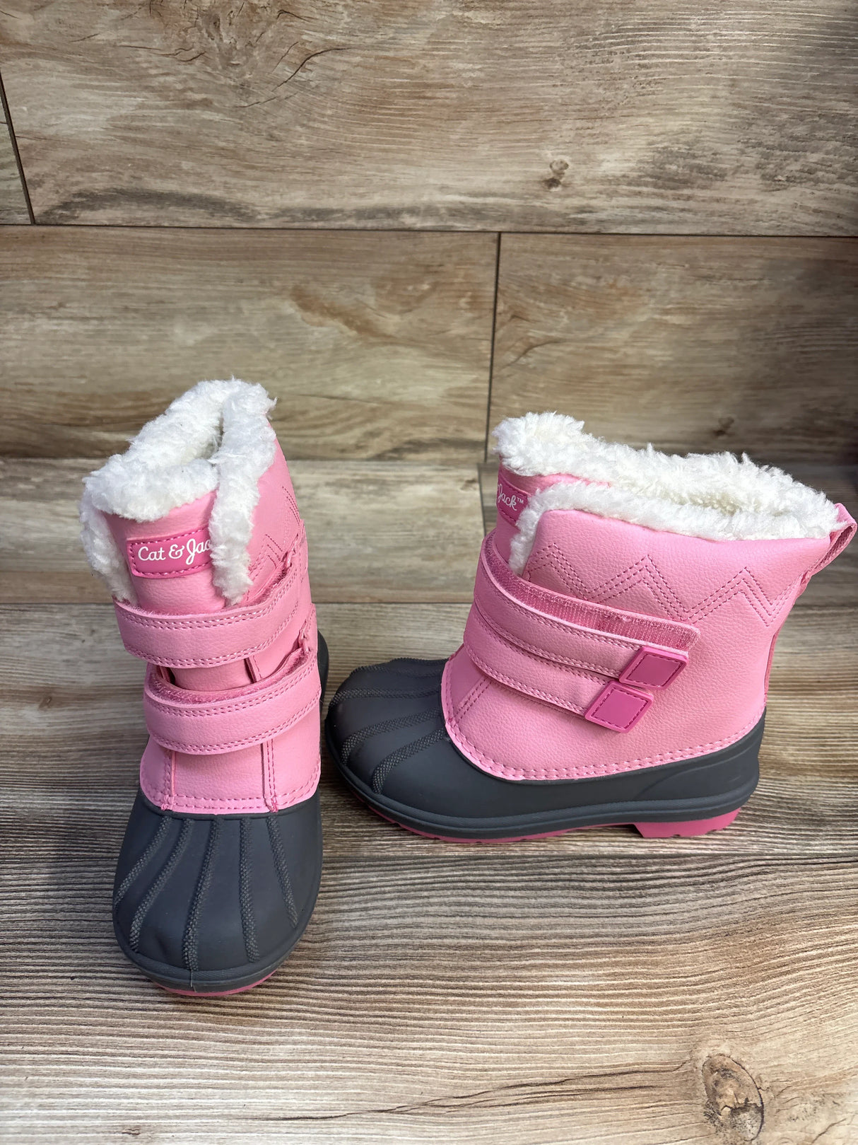 Front three-quarter view of Cat and Jack pink toddler winter boots size 12C showcasing white faux-fur lining, double Velcro straps, and gray rubber toe on wood background