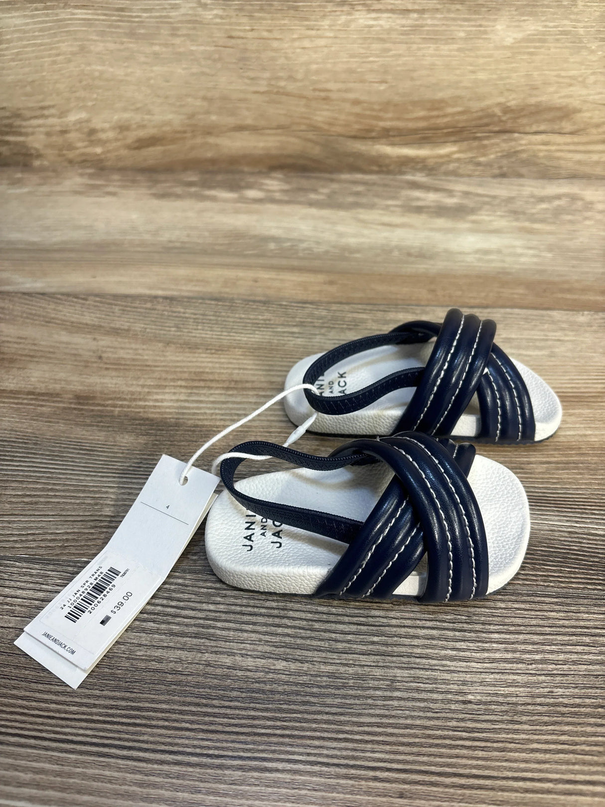Navy blue and white baby sandals with crisscross straps and price tag on wood surface