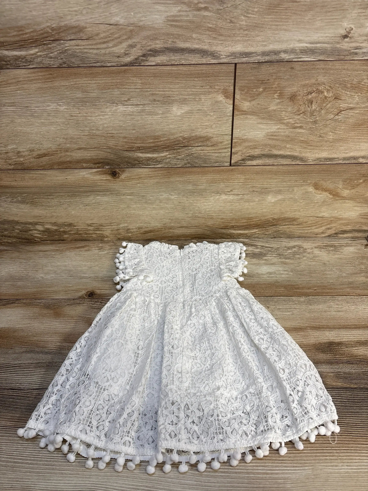 White lace toddler dress with pom pom trim on wooden background, gently used kids clothing