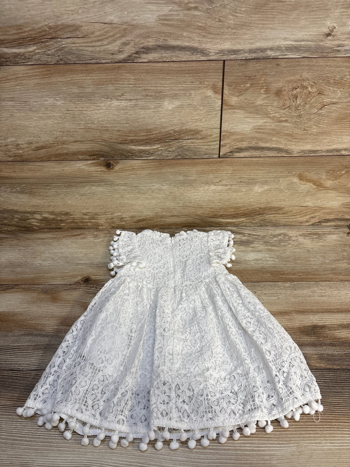White lace toddler dress with pom pom trim on wooden background, gently used kids clothing