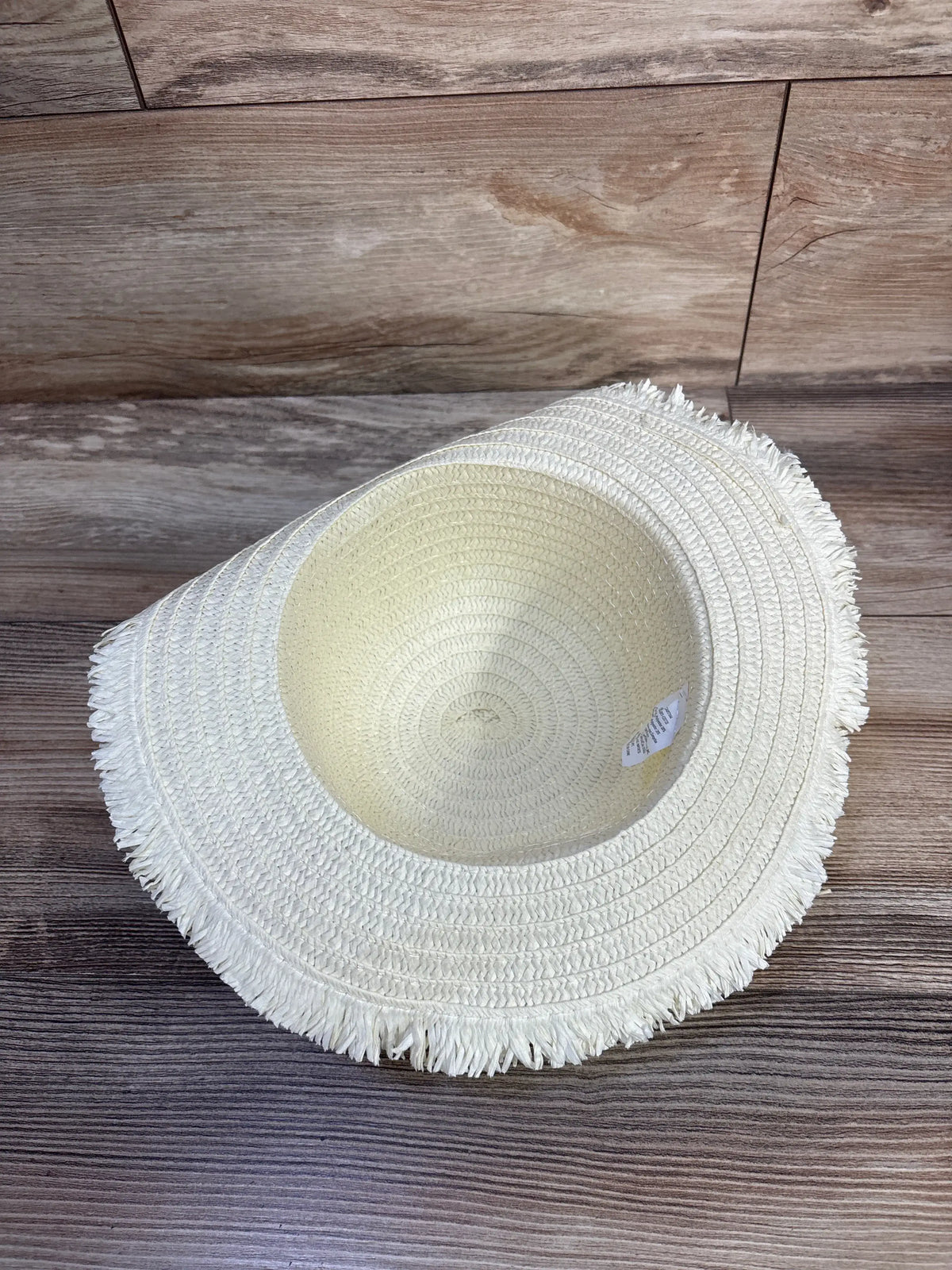 Interior view of Juncture floral straw bucket hat showcasing woven construction and fringed brim on wood-grain flooring