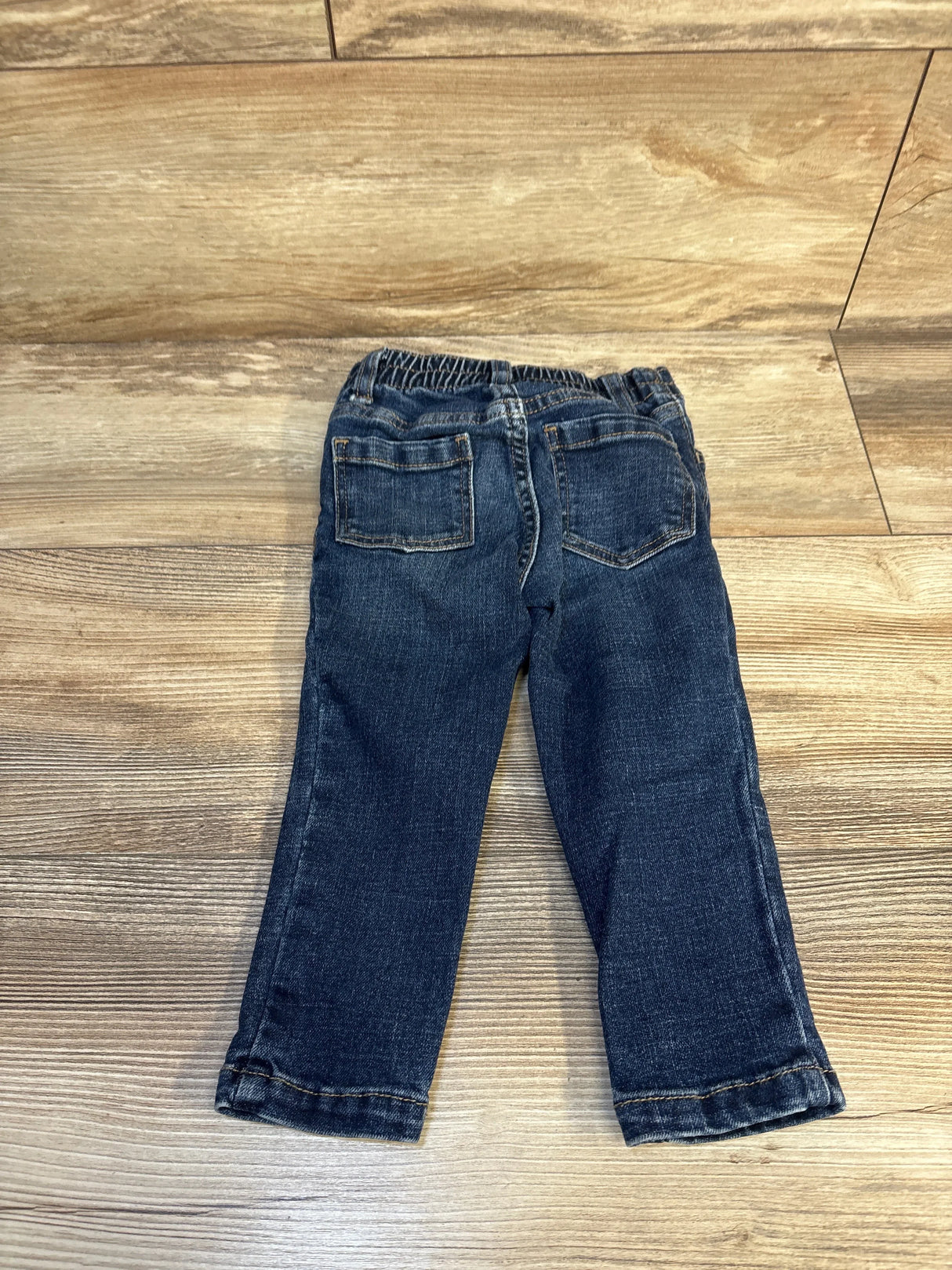 Toddler dark wash denim jeans with elastic waistband and back pockets on wood floor