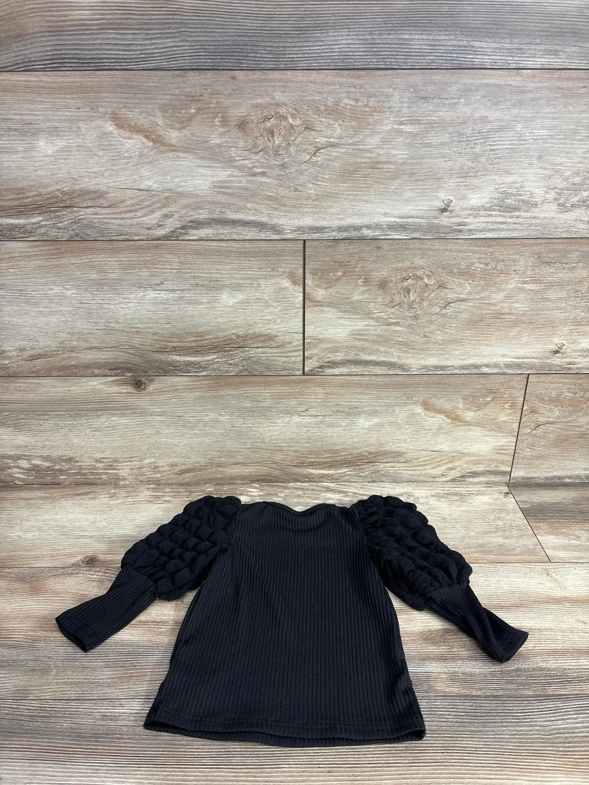 Black ribbed long sleeve girl’s top with textured puff sleeves on wood background