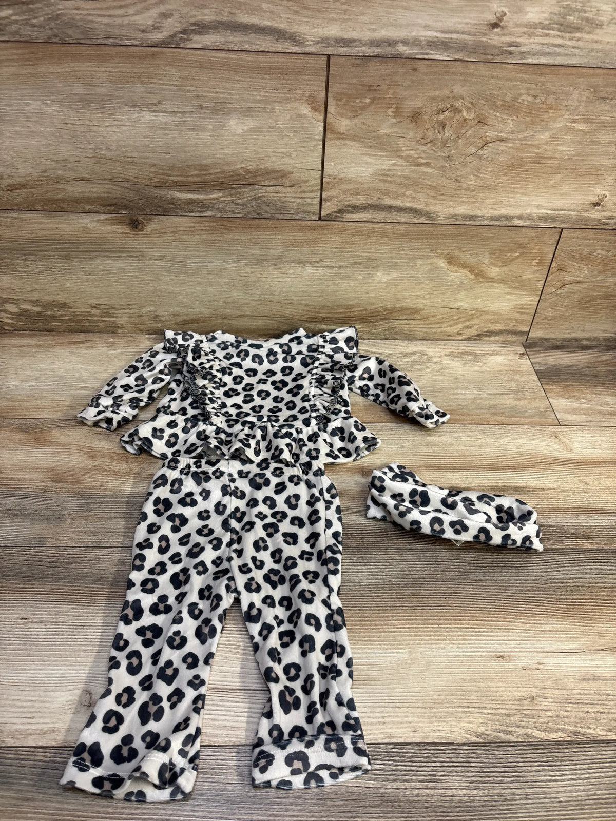 Top-down of Floral Threads tan leopard-print layette set with ruffled top, elastic-waist pants, and headband on wood floor