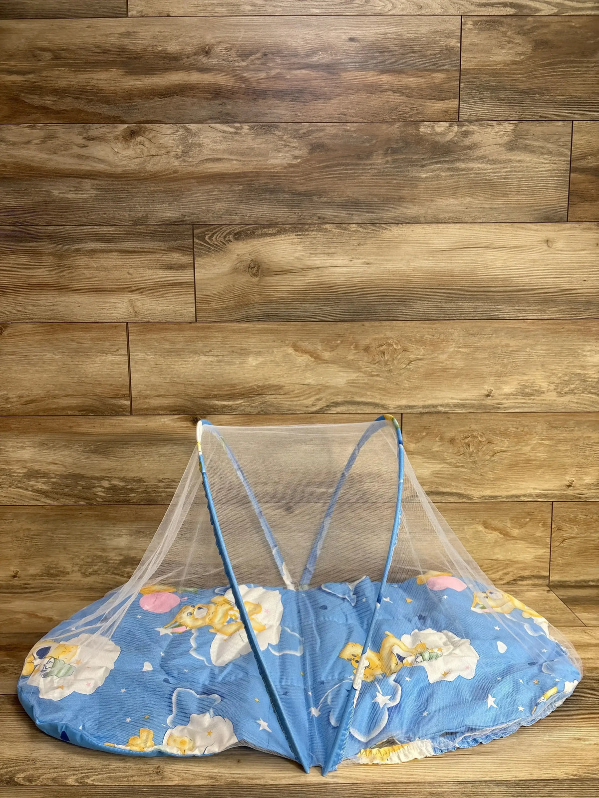 Blue baby mattress with cartoon bear print and protective white mesh netting on wooden floor