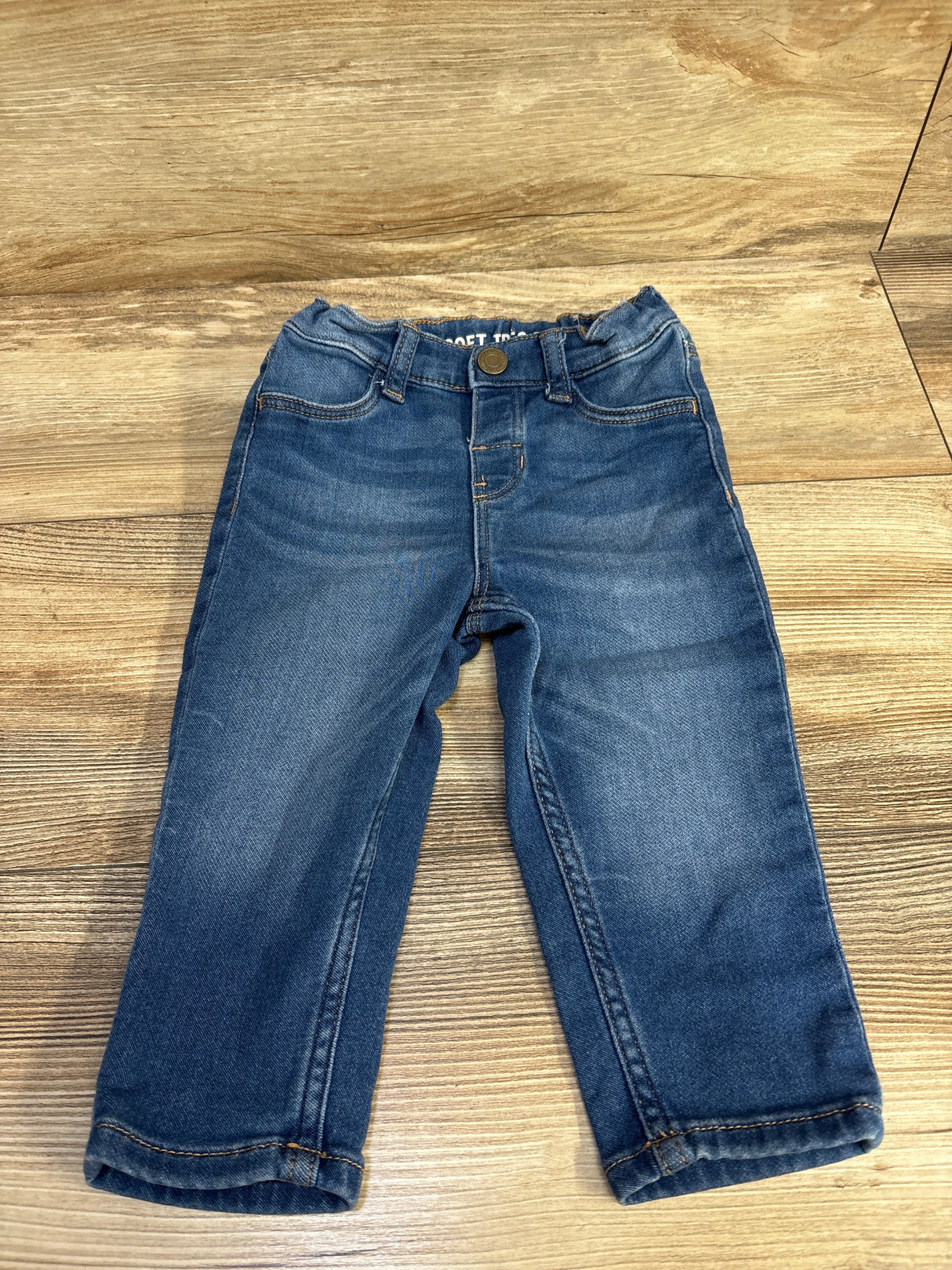 Toddler blue denim jeans with button waist on wood floor