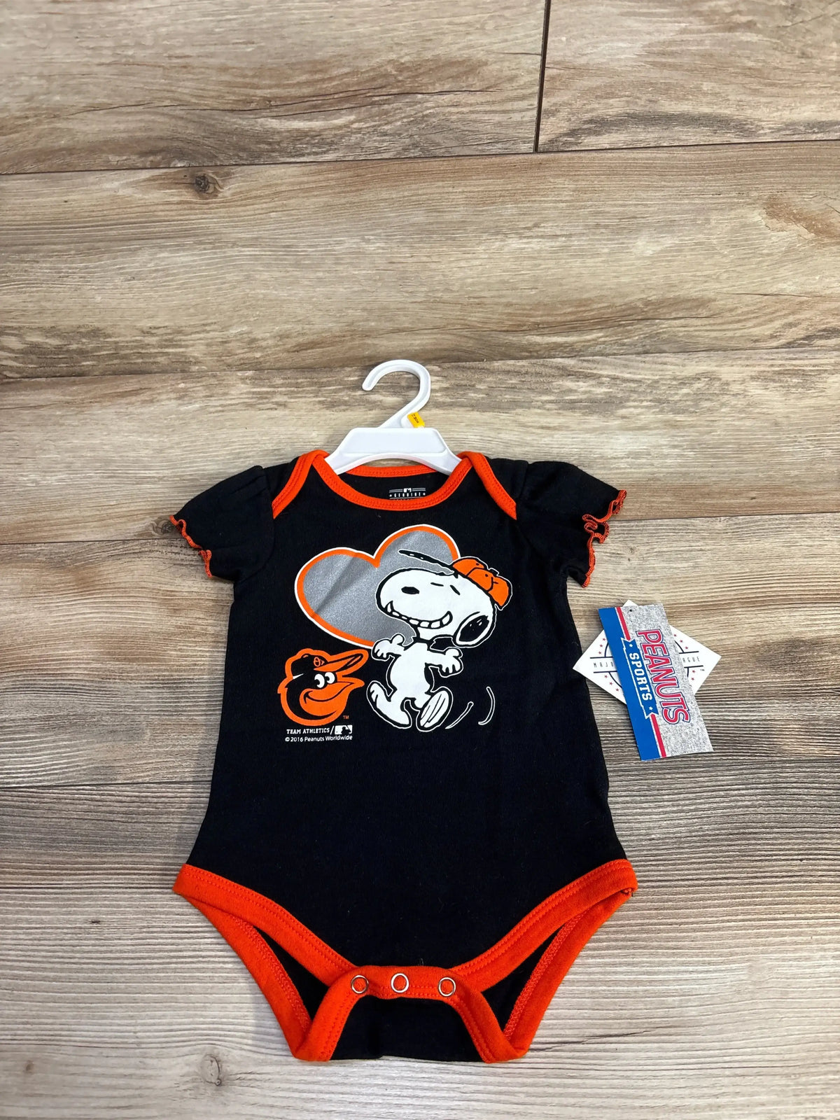 Black baby onesie with Snoopy and Baltimore Orioles logo, orange trim, on wood floor