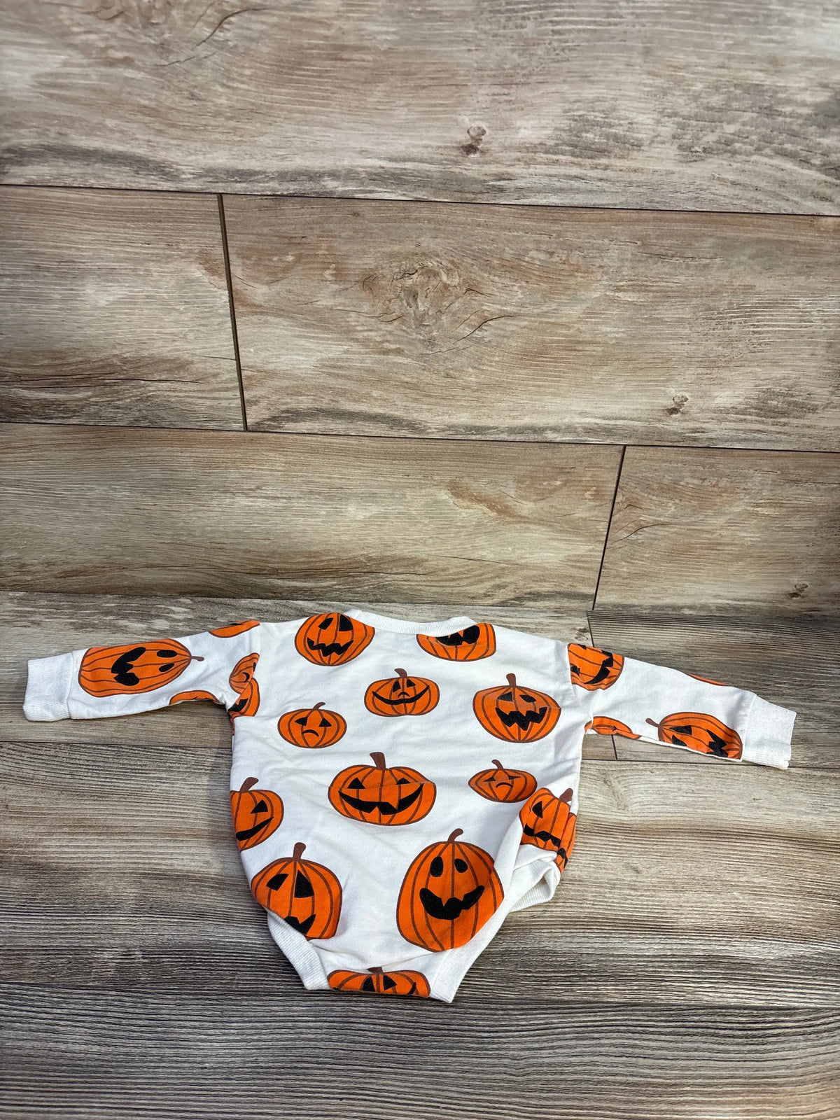 Front view of cream pumpkin patch bubble romper showcasing long sleeves, bubble leg detailing, and pumpkin print on a wood floor