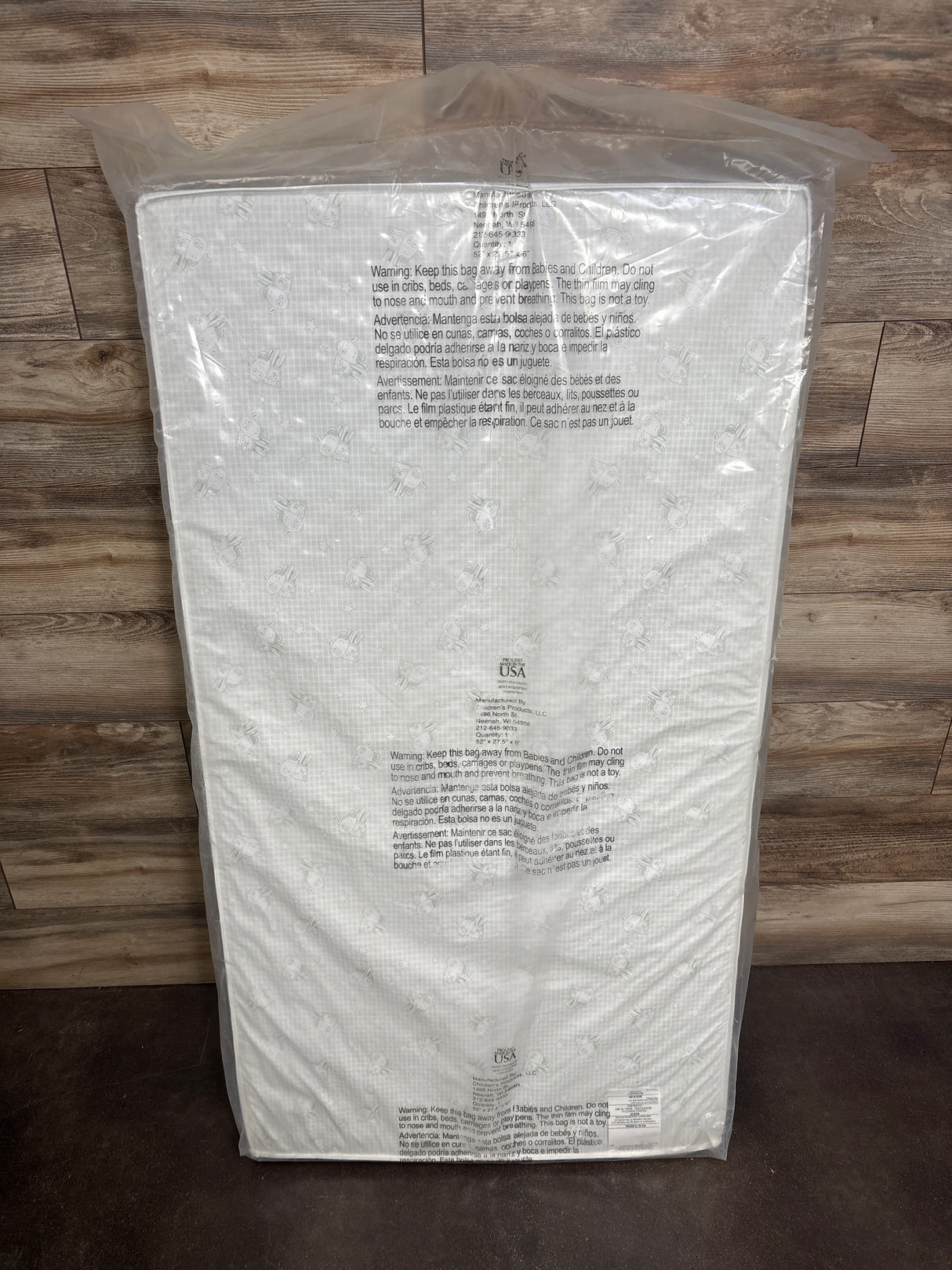Top view of NEW Serta Perfect Slumber Dual Sided Crib and Toddler Mattress in white sealed plastic packaging on a wood plank background