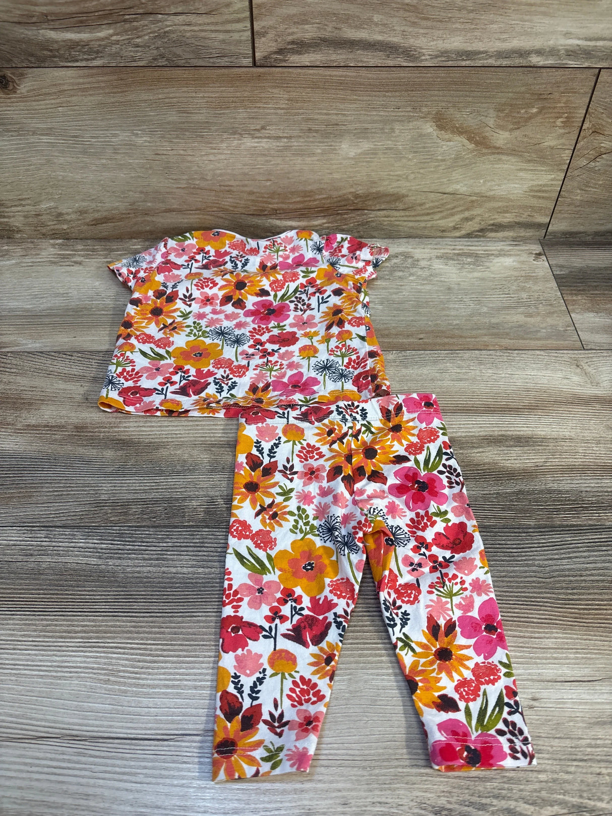 Flat lay of Fred and Flo floral 2-piece newborn pajama set showing short sleeve top and matching leggings on wood floor