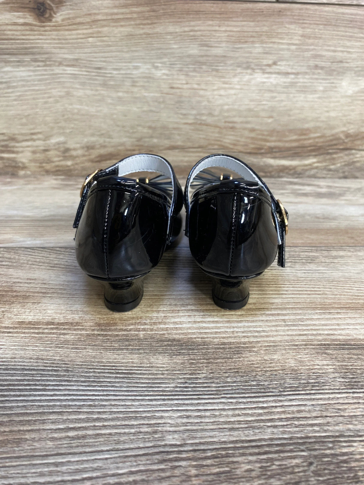 Rear view of black patent leather kids dress shoes with buckle straps on wood floor