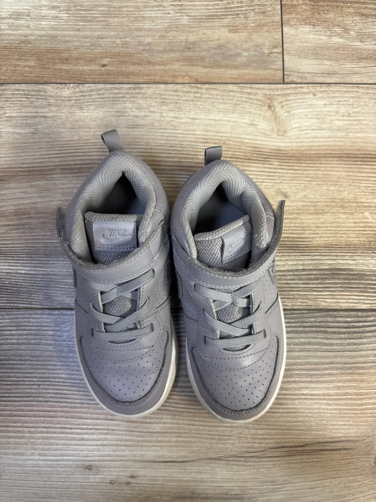 Top view of Nike Court Borough Mid toddler sneakers showing mid-top silhouette, Velcro strap and perforated toe on light wood floor