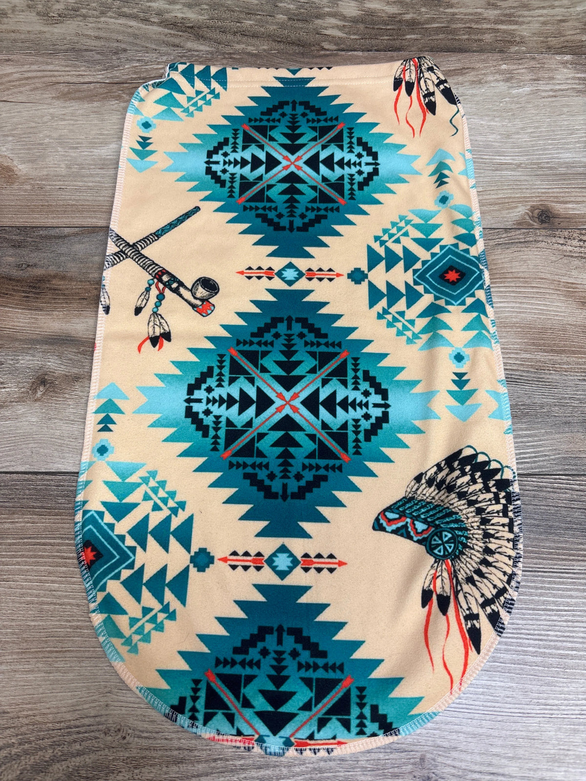 Top view of beige Native Design Swaddle Sack featuring turquoise, black, and red geometric pattern with feather motifs on wood floor