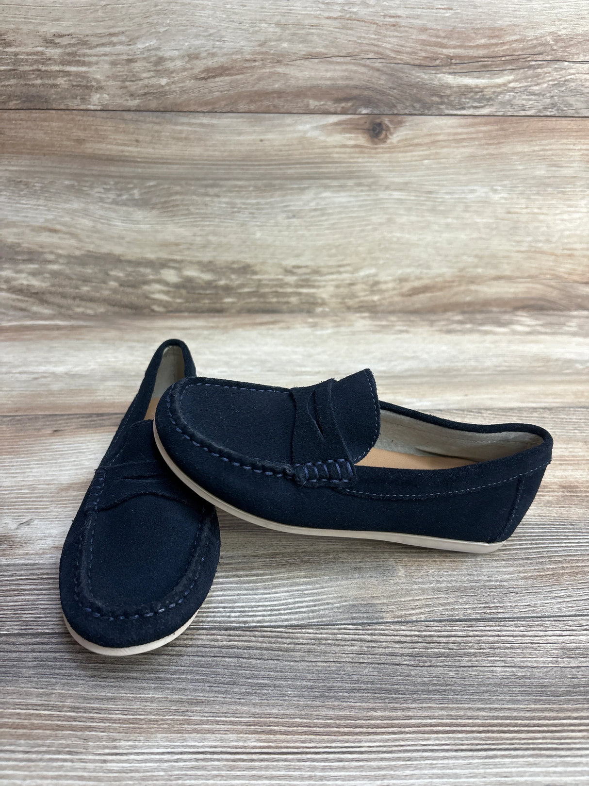 Black suede penny loafers with light soles on wood background