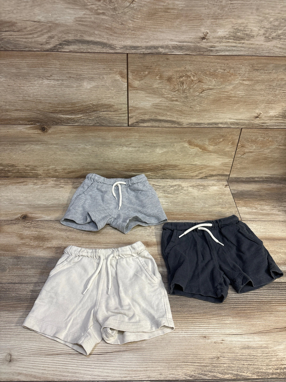 Flat lay of three Old Navy toddler drawstring shorts size 12-18m showcasing elastic waistbands and front drawstrings on wood background