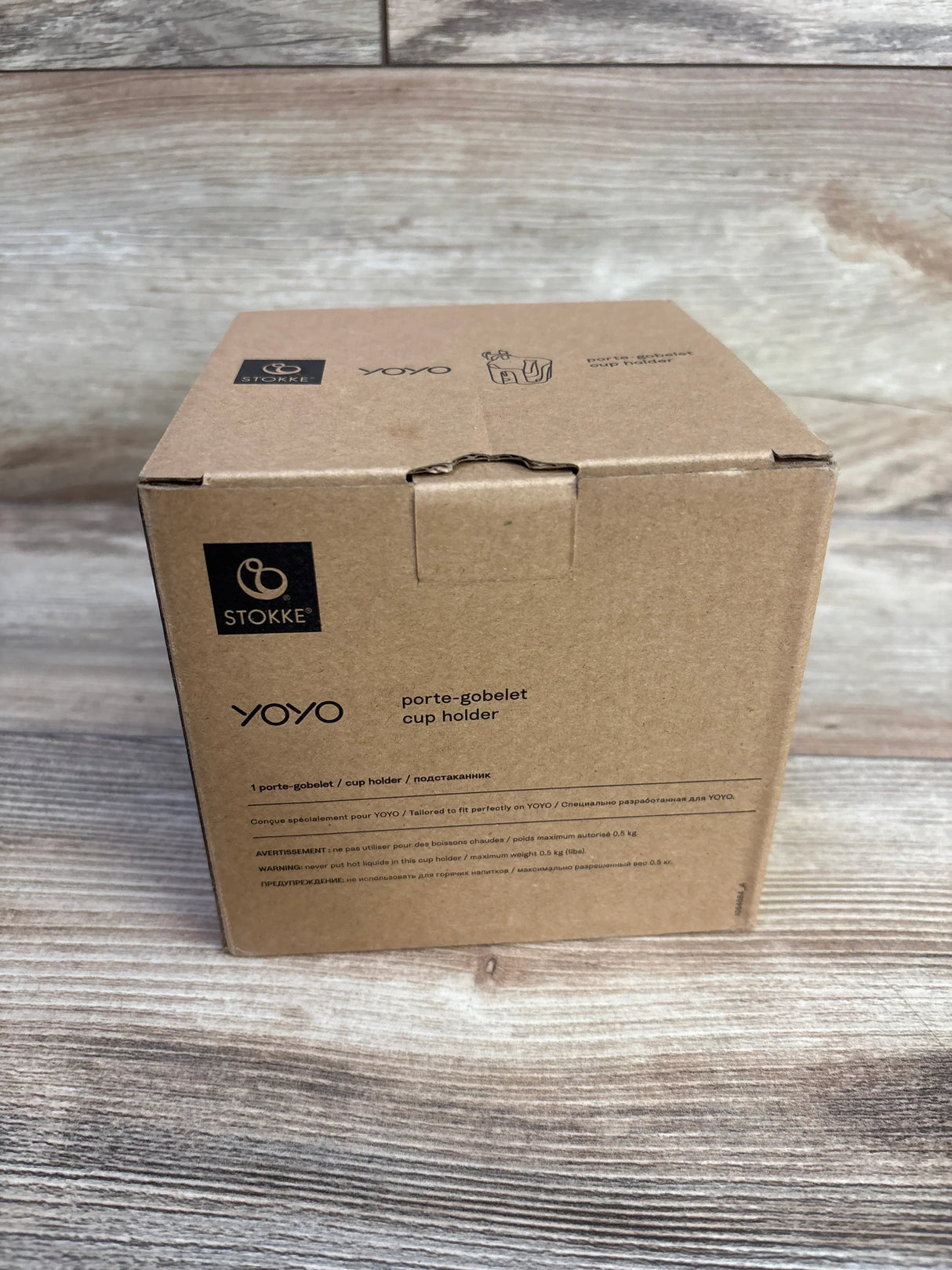Front view of boxed Stokke YOYO stroller cup holder (black) showing Stokke logo and product label on a wood surface